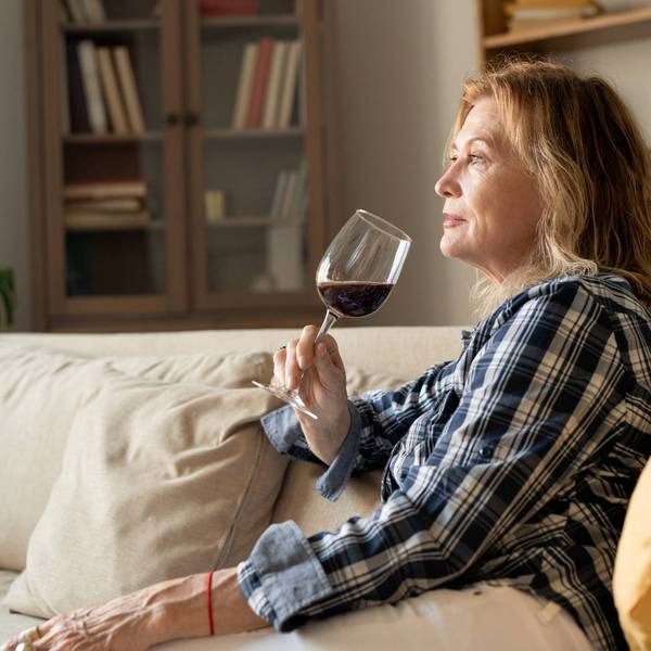 female with glass of red wine leaning against soft pillow while sitting on couch