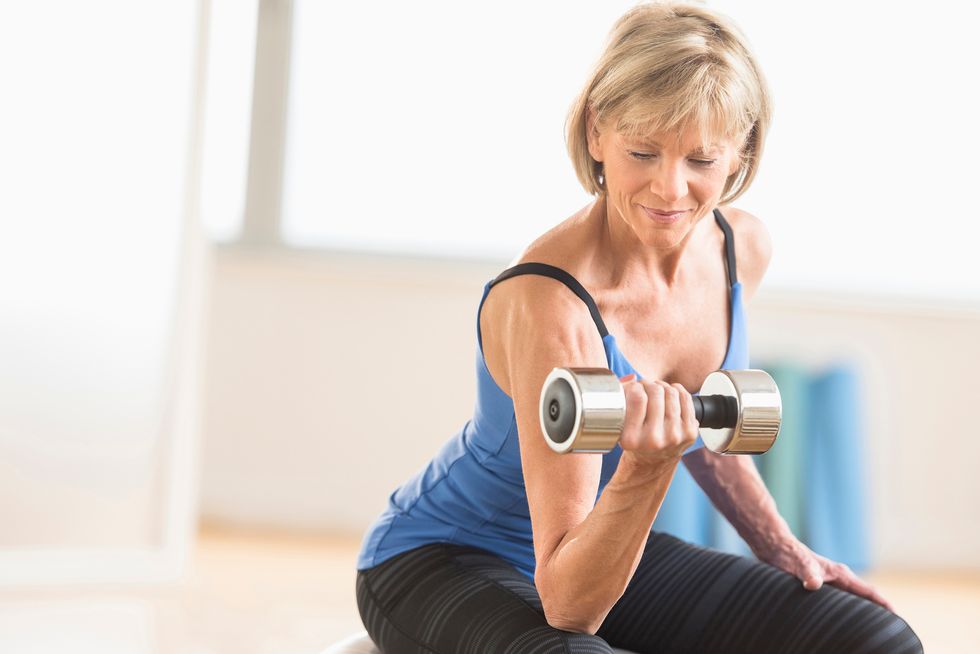 Fit mature woman lifting dumbbell while sitting at home