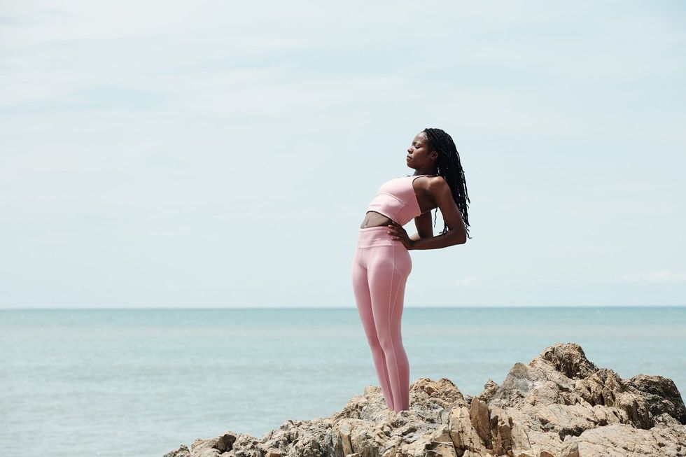 Fit young woman doing exercises on sharp rocks at the seaside