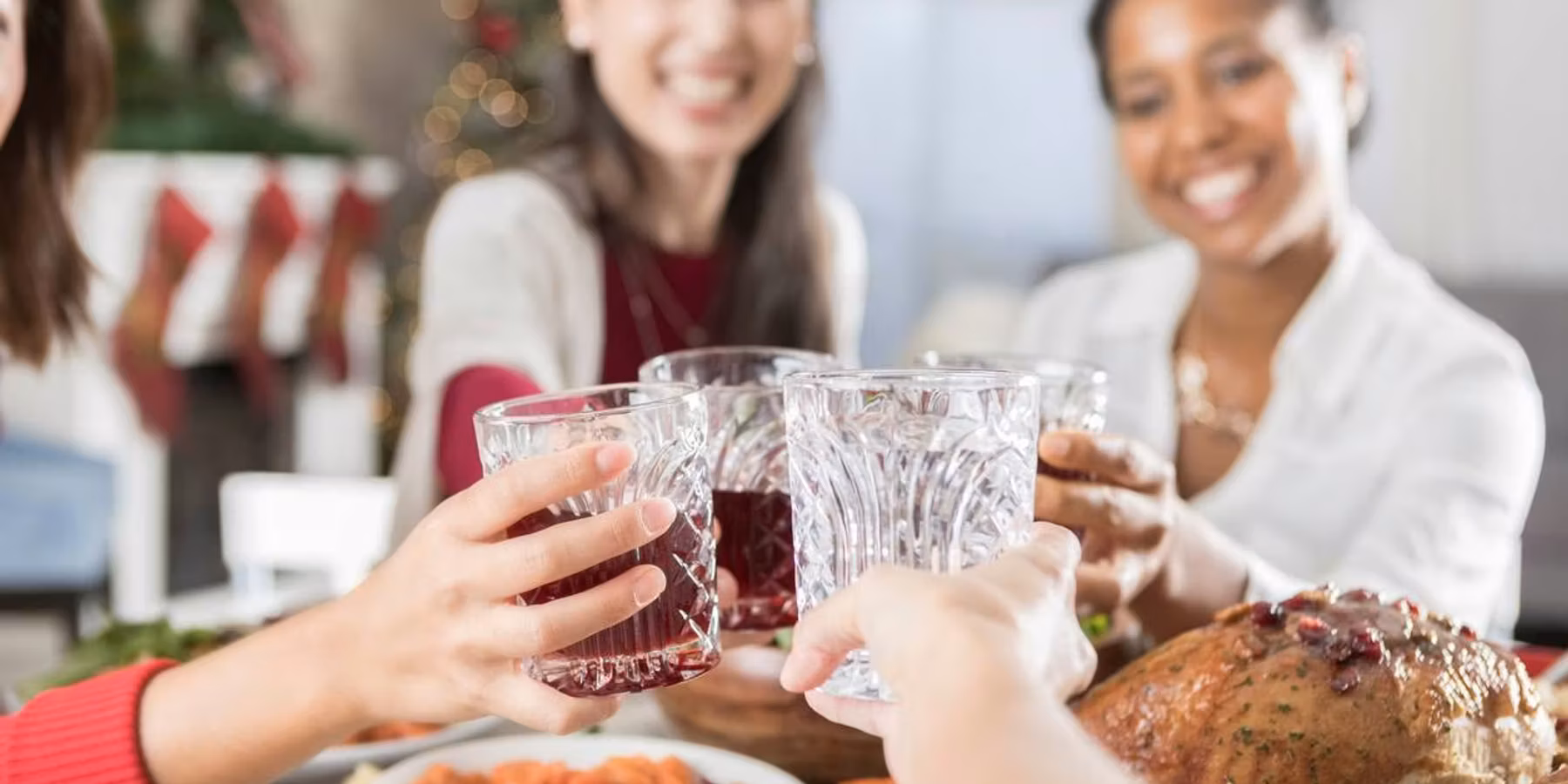 four drinking glasses as they are clinked above a full Christmas dinner table