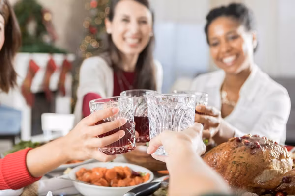 four drinking glasses as they are clinked above a full Christmas dinner table