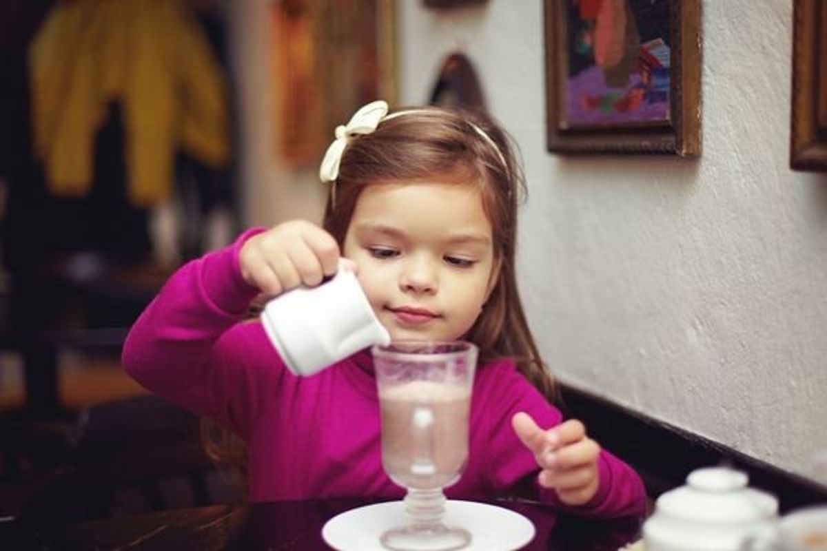 girl pouring milk into coffee