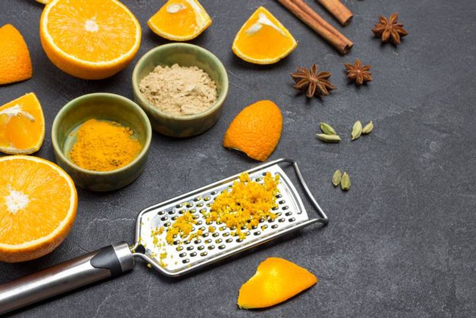 Grated orange peel on grater. Sliced orange and spices on table