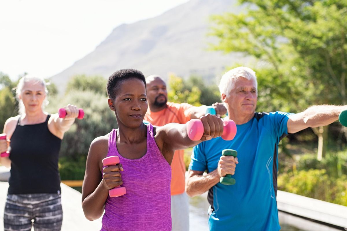 Group of mature adults exercising with dumbbells outside with a mountain view.