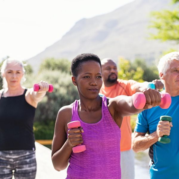 Group of mature adults exercising with dumbbells outside with a mountain view.