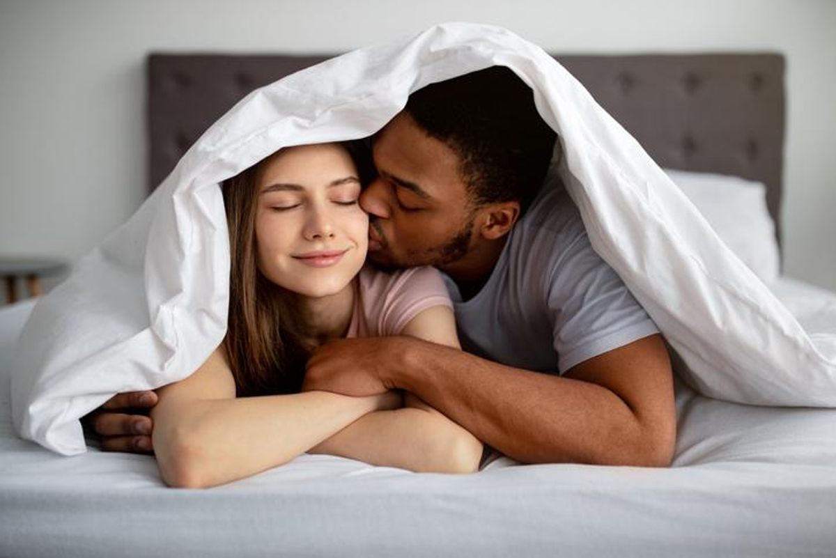 guy kissing his girlfriend under blanket on bed