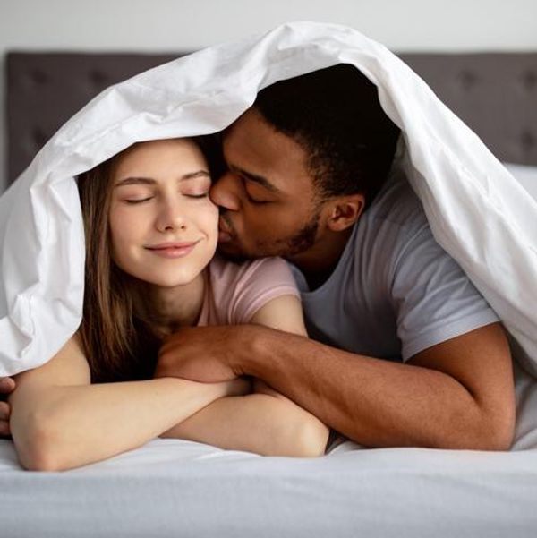 guy kissing his girlfriend under blanket on bed