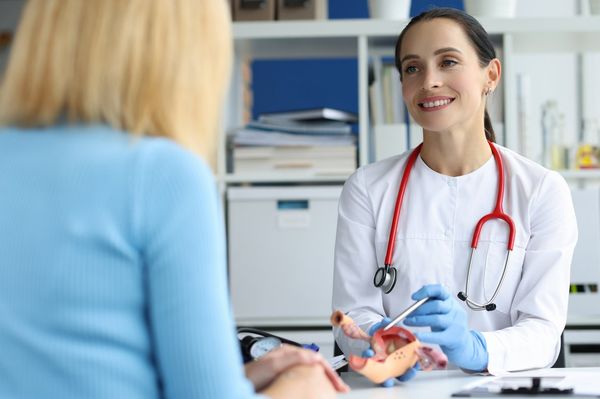 Gynecologist holds model of female reproductive system of uterus and consults patient.