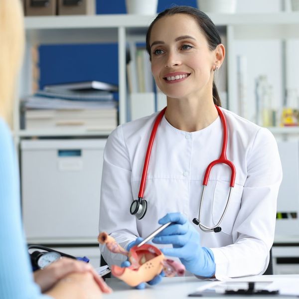 Gynecologist holds model of female reproductive system of uterus and consults patient.
