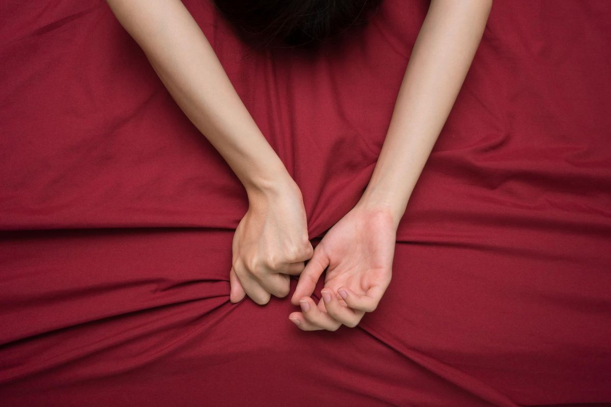 Hand grasping on bed sheet, woman having trouble orgasming
