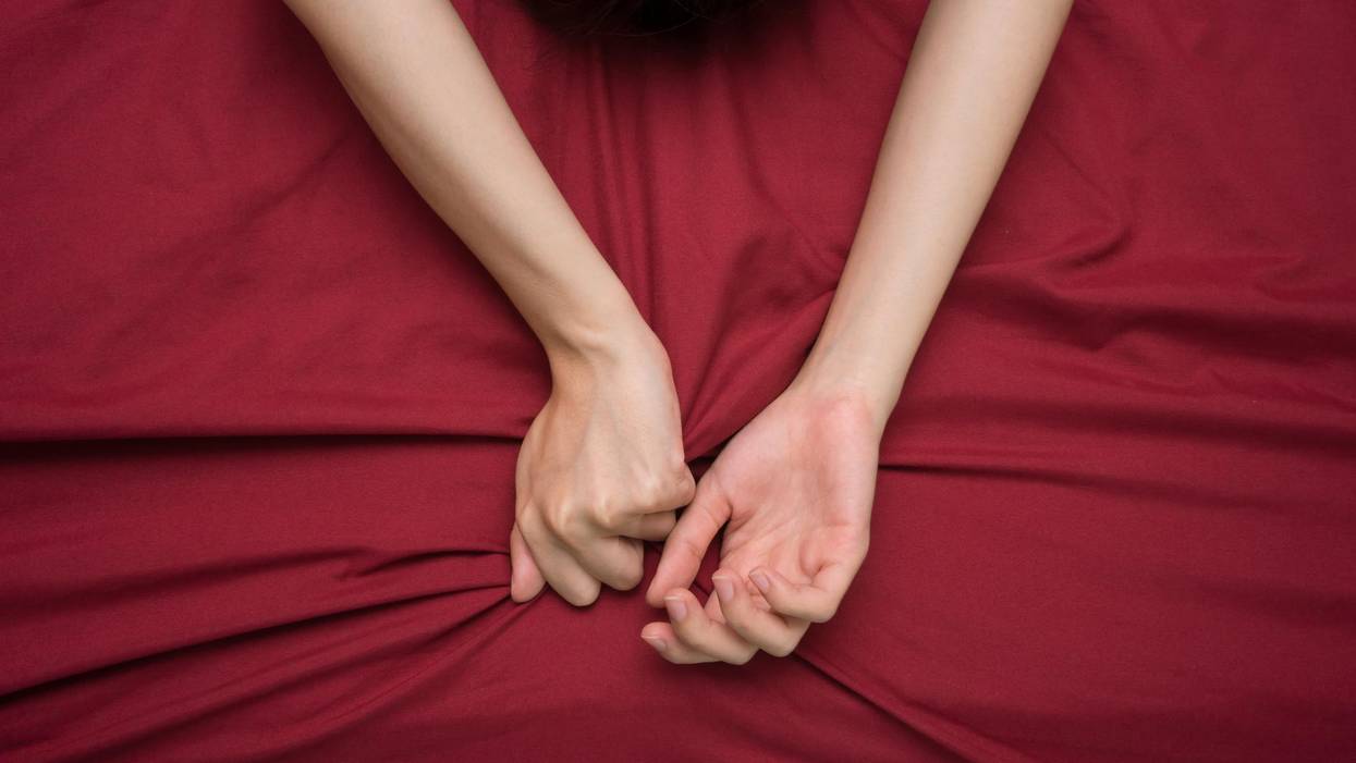 Hand grasping on bed sheet, woman having trouble orgasming