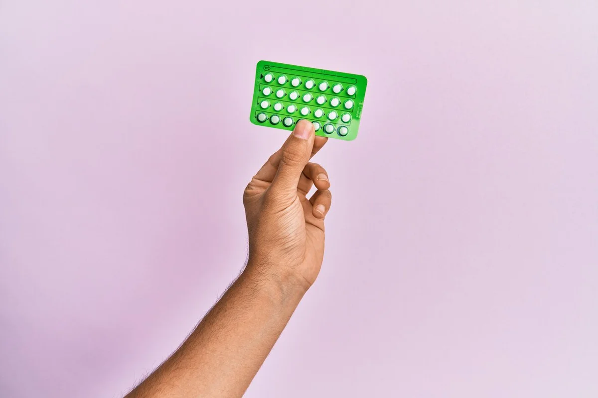 hand holding birth control pills over isolated pink background.