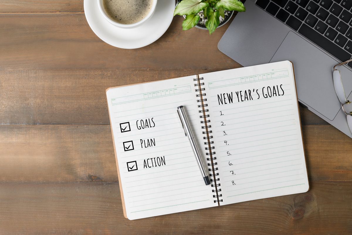 Hand writing New year's goals on note paper with coffee and laptop