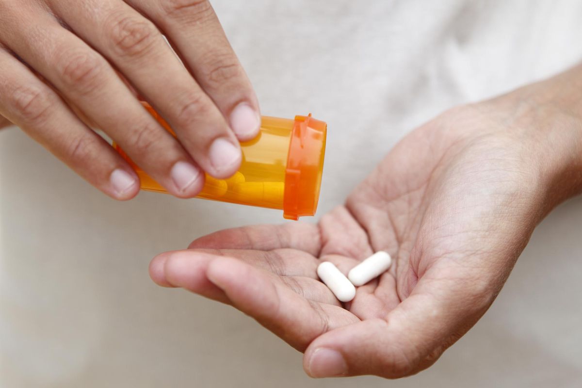 Hands holding an orange pill bottle pouring two pills into palm.