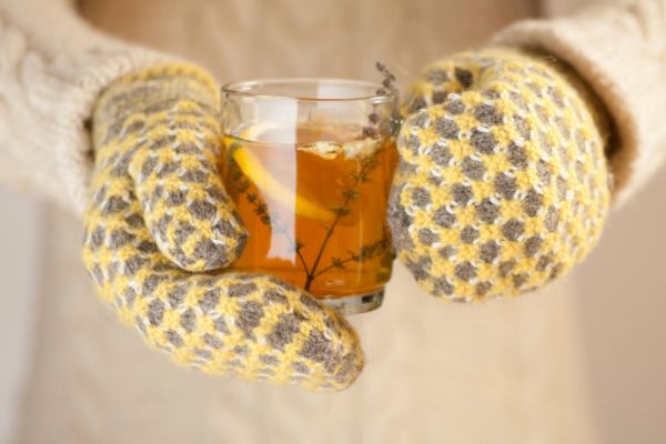 Hands in knitted mittens holding a cup of herbal tea with lemon on a cold day