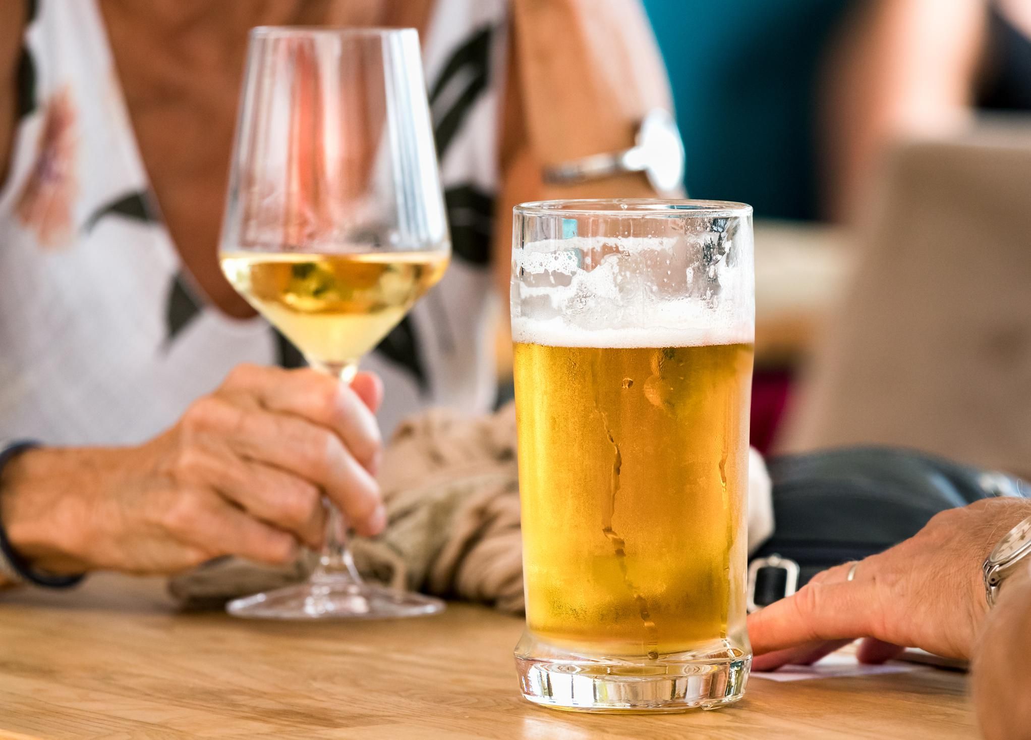 Hands of a couple with beer and white wine sitting at a table outdoors