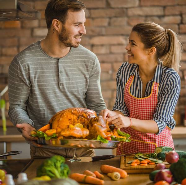 happy couple communicating while preparing Thanksgiving turkey for dinner at dining room