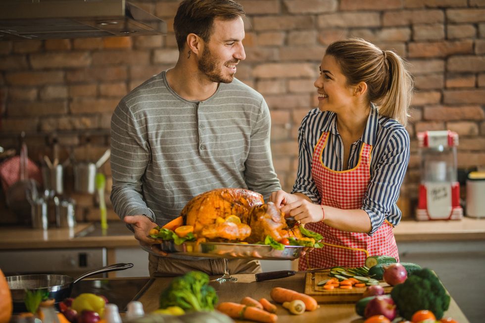happy couple communicating while preparing Thanksgiving turkey for dinner at dining room