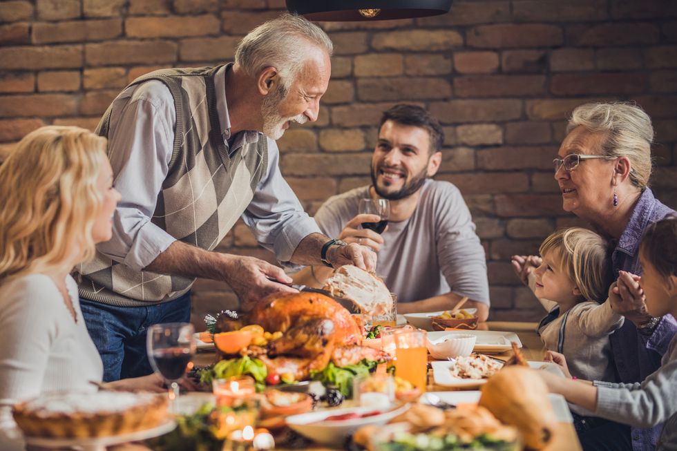 Happy extended family talking on Thanksgiving dinner at dining table, while senior man is carving meat.