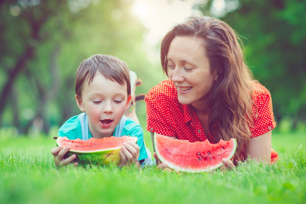 Happy little boy and his mother eating watermelon in a park