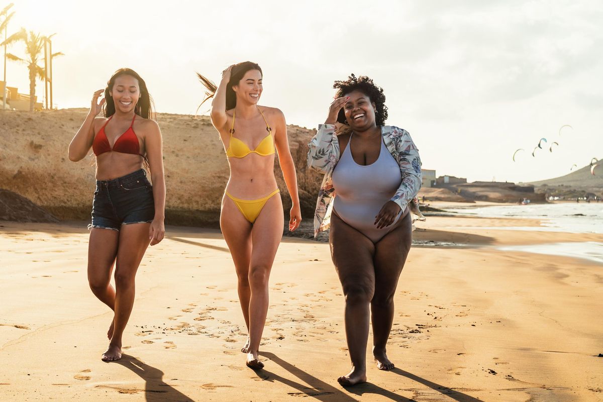 Happy multiracial females with different body size having fun walking on the beach