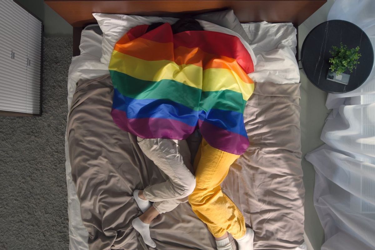 homosexual partners cuddle in bed covered with lgbt flag