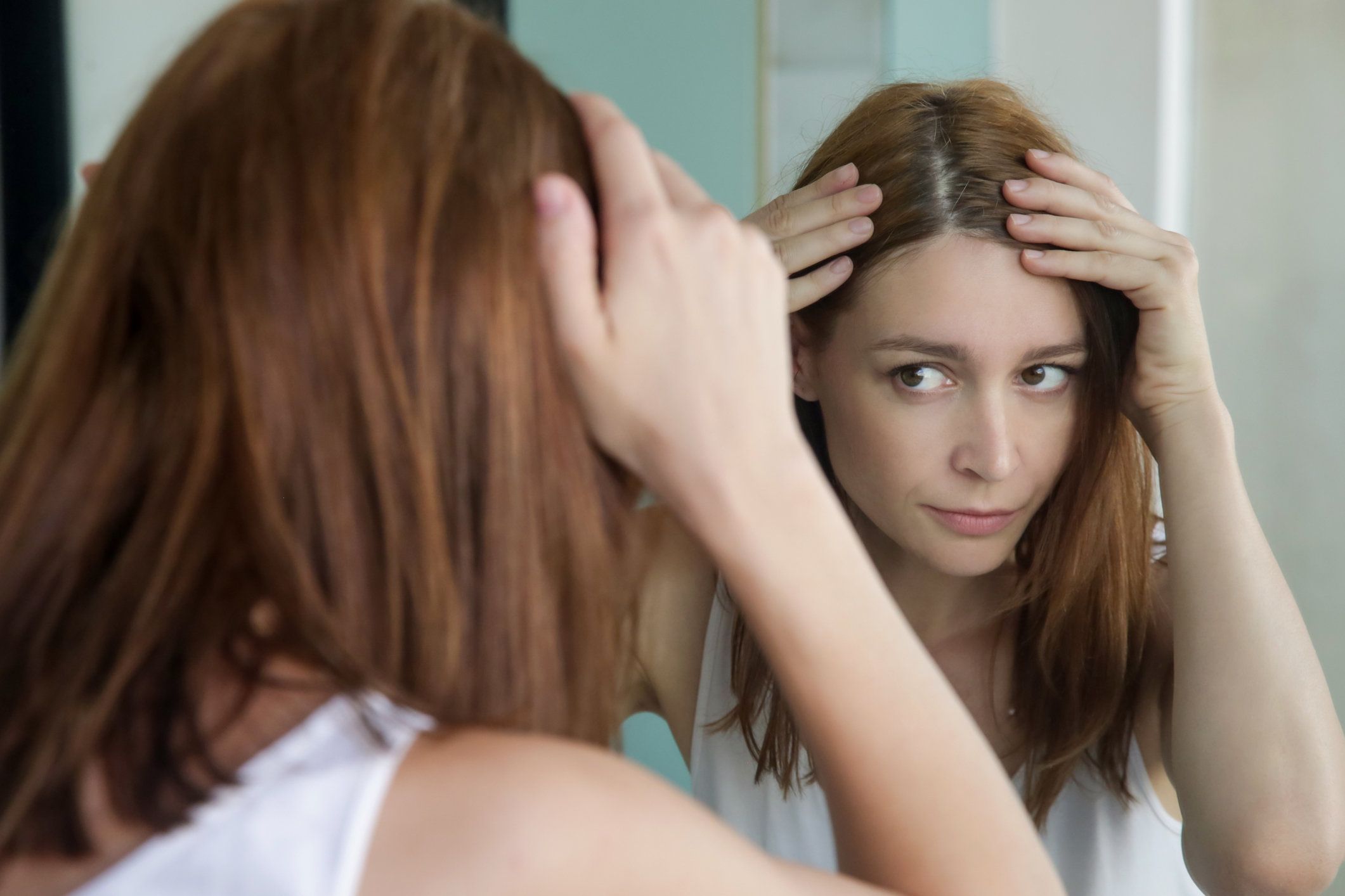 woman examining her scalp and hair in front of the mirror for hair loss
