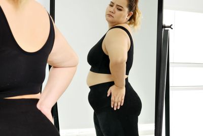 obese woman standing and looking at her stomach in a mirror