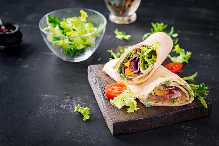 Fresh tortilla wraps with ham beef and fresh vegetables on wooden board