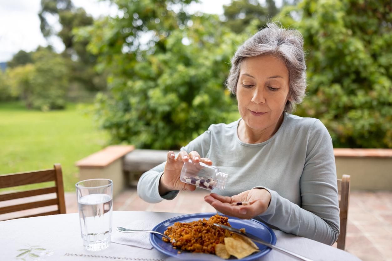Senior woman taking her medicines with food while eating lunch