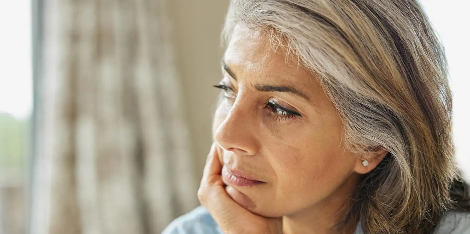 Imagen de una mujer madura pensativa mirando por la ventana.