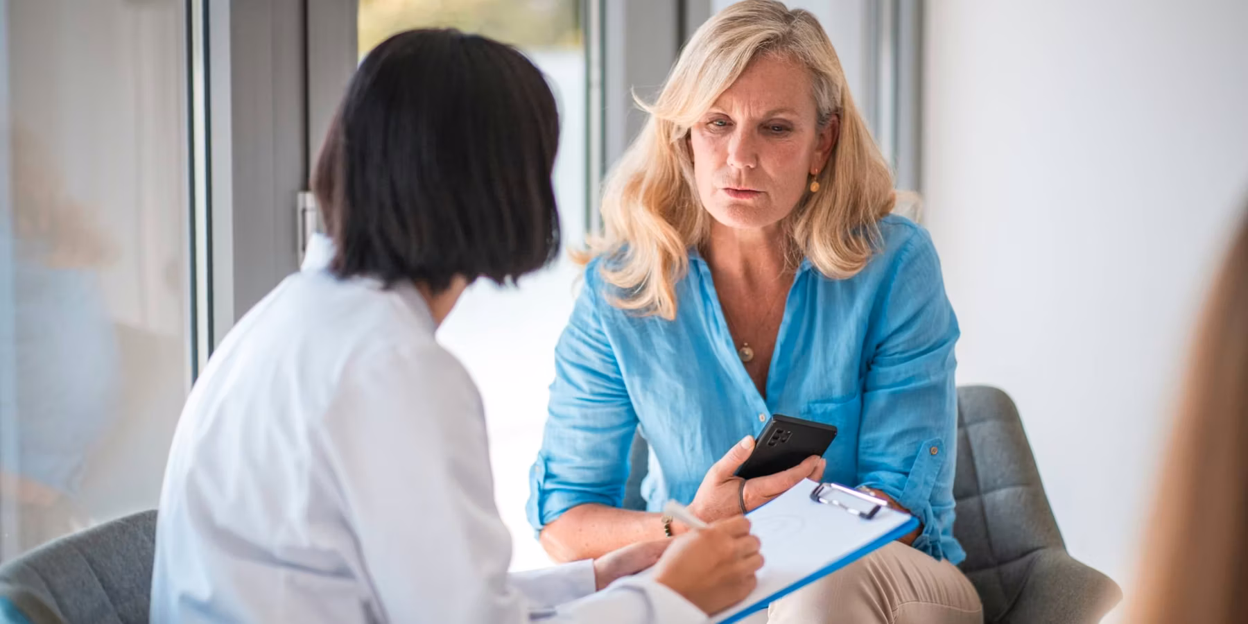 In a doctor's office with a mature Caucasian female patient and an Asian female doctor.