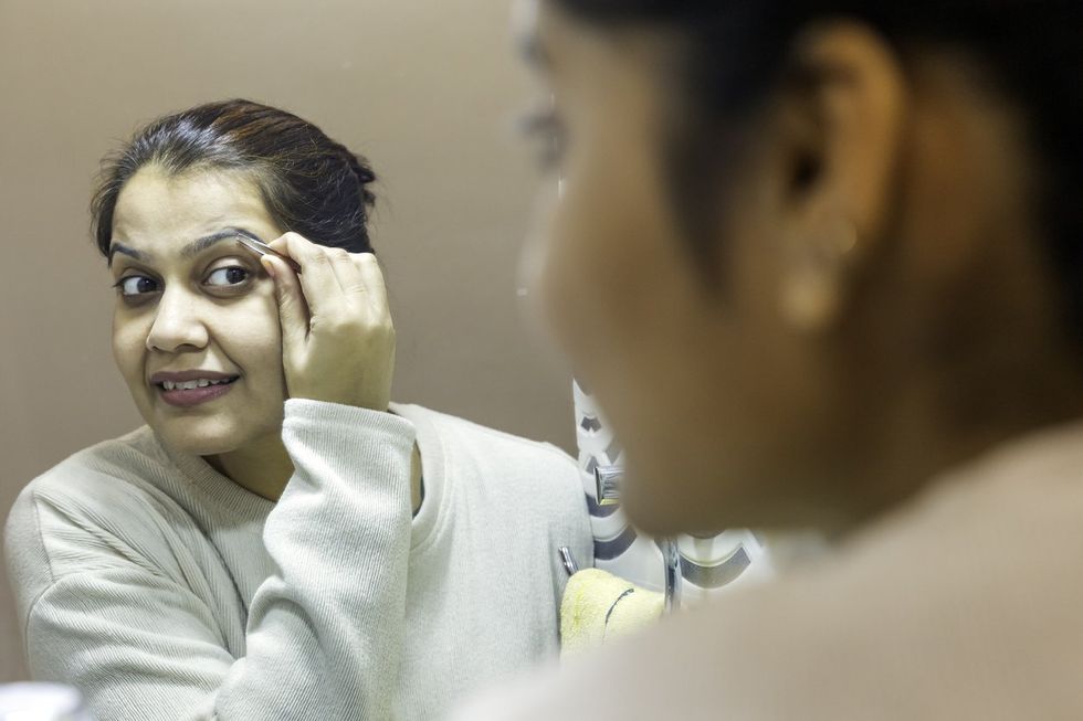 Indian woman look in mirror plucking eyebrows. using metal tweezer
