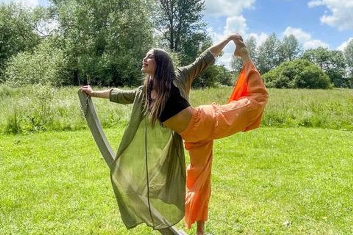 Kim Booker doing a yoga pose outside with green grass and trees.