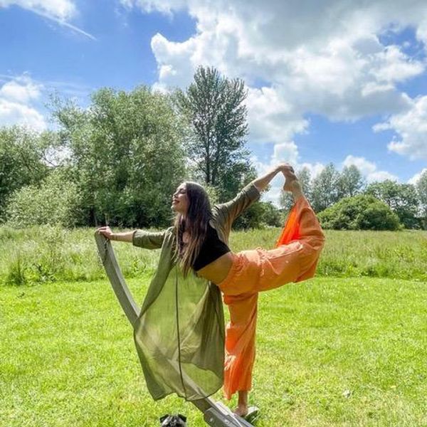 Kim Booker doing a yoga pose outside with green grass and trees.