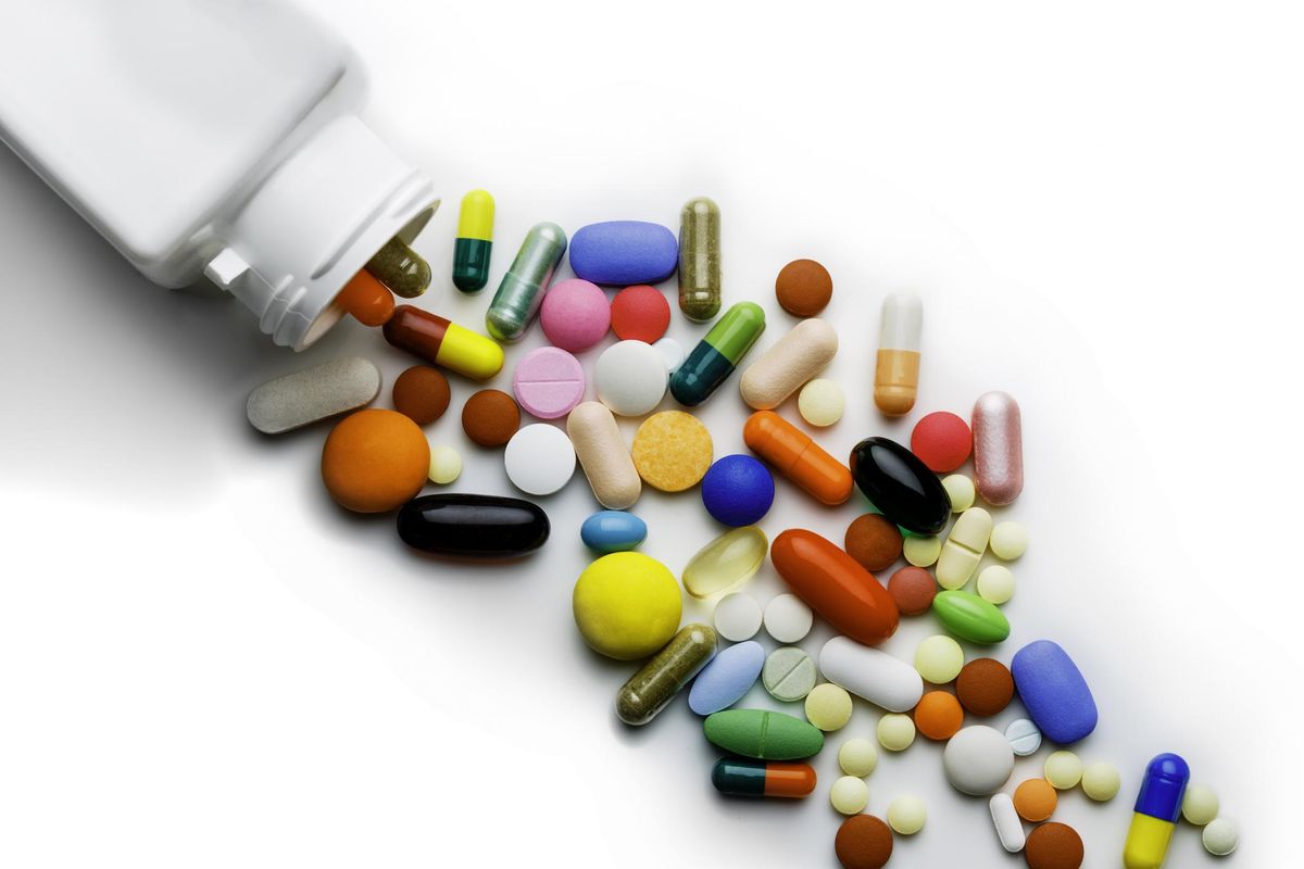 Large group of assorted capsules and pills coming out from bottle on a on white background