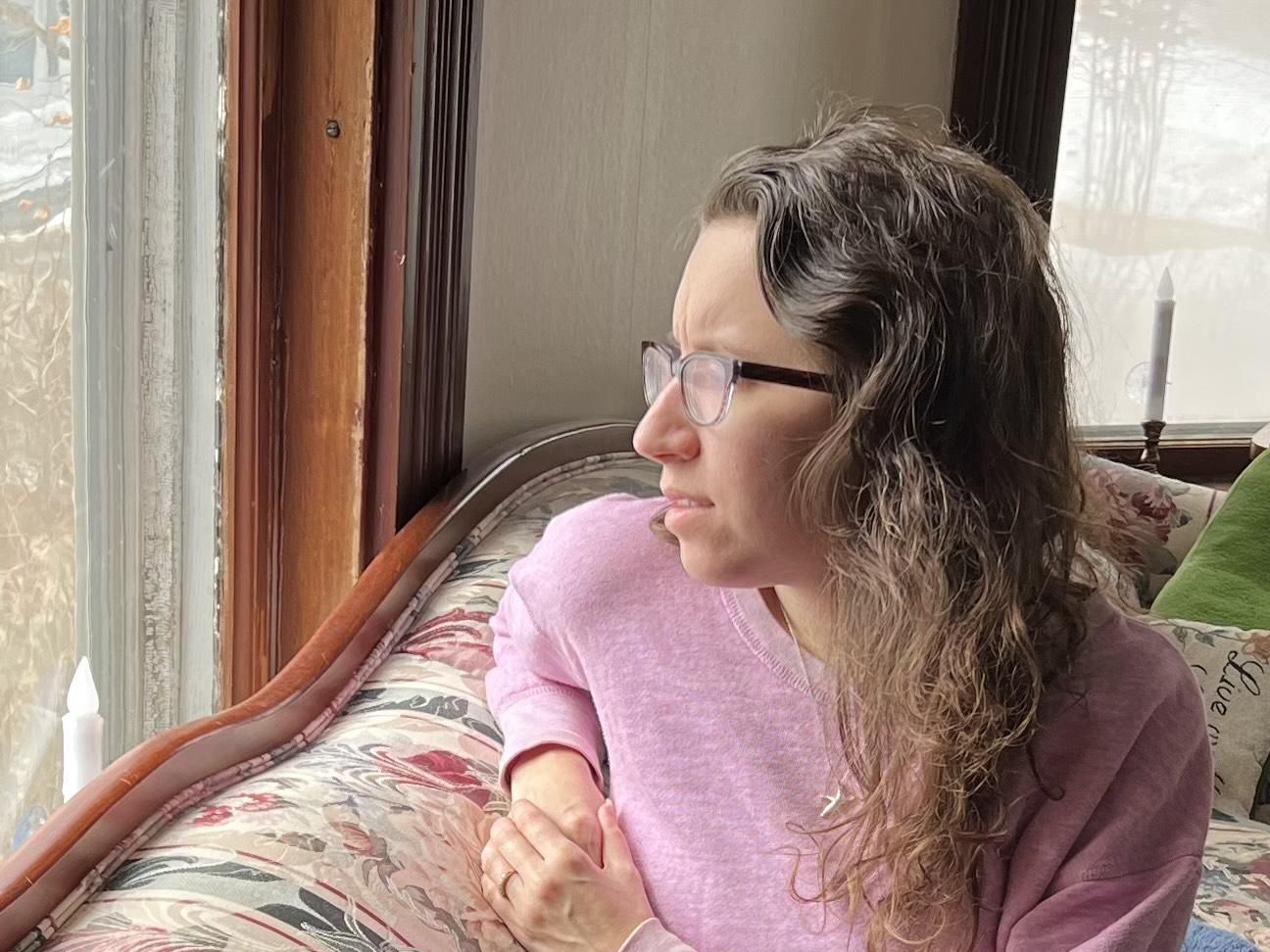 Liz looking out of the window wearing a pink sweater on a floral couch