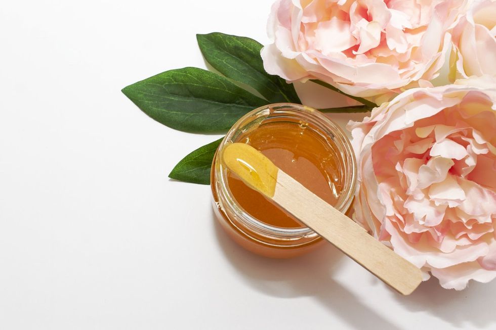 Liquid sugar paste for hair removal in a bowl with peony flower on white background