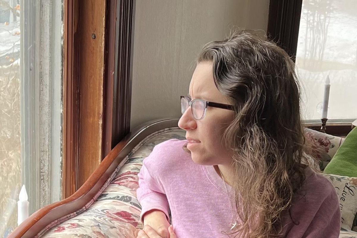 Liz looking out of the window wearing a pink sweater on a floral couch