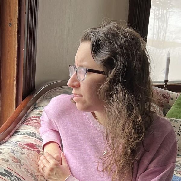 Liz looking out of the window wearing a pink sweater on a floral couch