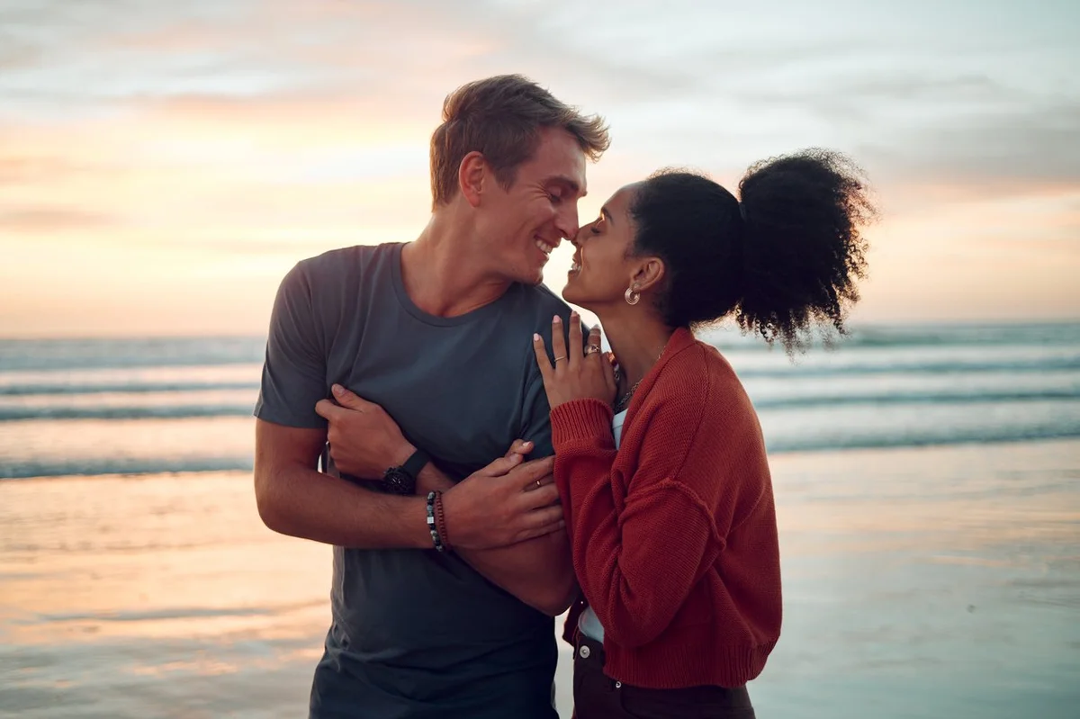 Love, beach and couple kiss at sunset, happy and bonding on their summer vacation in Florida. Travel, freedom and romance with man and woman enjoying a walk along the ocean and showing affection