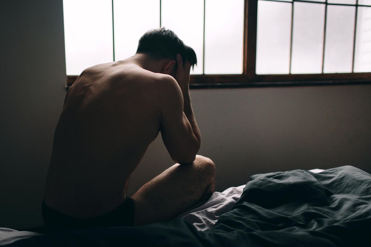 Man sitting on the edge of the bed looking upset holding his head in his hands