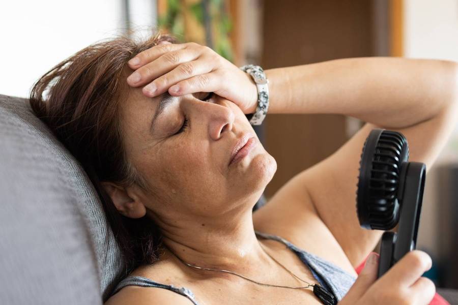 mature adult woman sweating and using a handheld electric fan