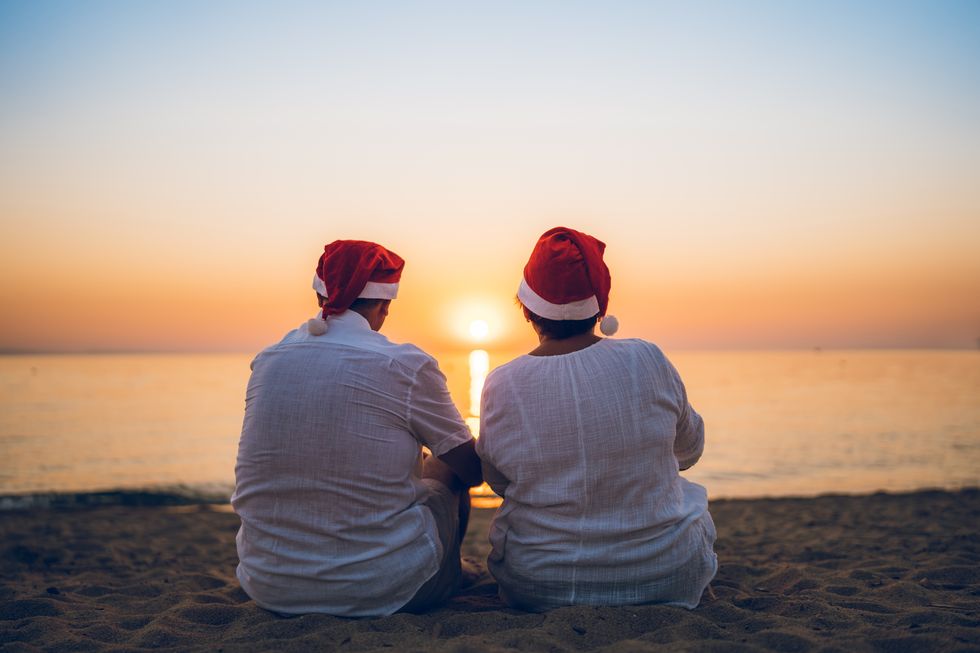 Mature couple with Santa hats watching sunset on the beach