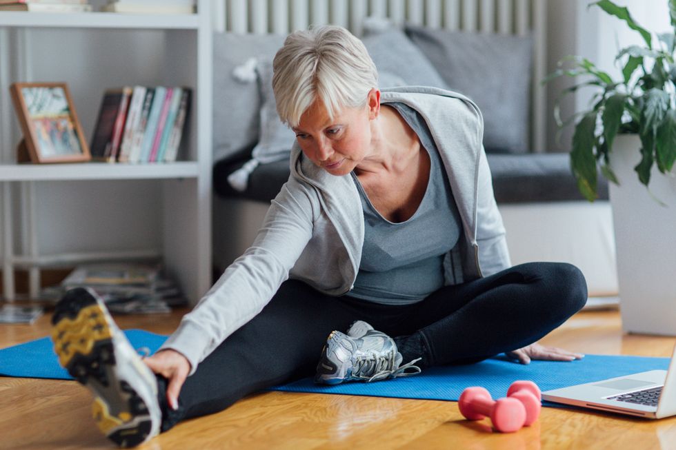 Mature woman exercising at home, learning exercises online with laptop