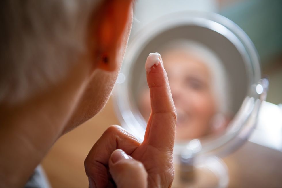 mature woman massaging her face while checking wrinkled eyes in the mirror