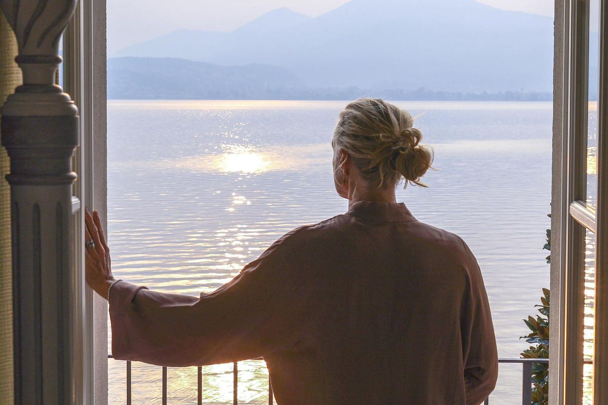 Mature woman walks out to veranda over a lake at sunrise