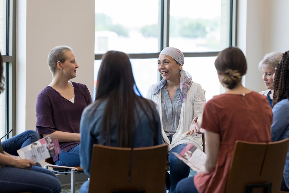 Mature woman wearing a headscarf gestures while discussing chemotherapy treatment with women in a breast cancer support group.