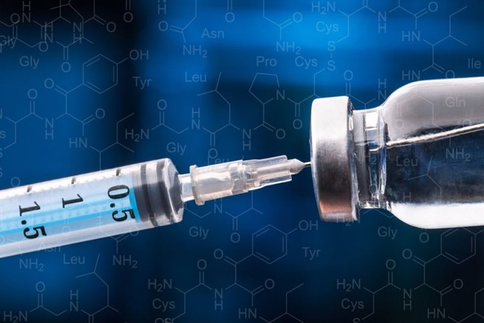 Medicininė ranka pirštinėje yra ampulė su vakcina ir švirkštu