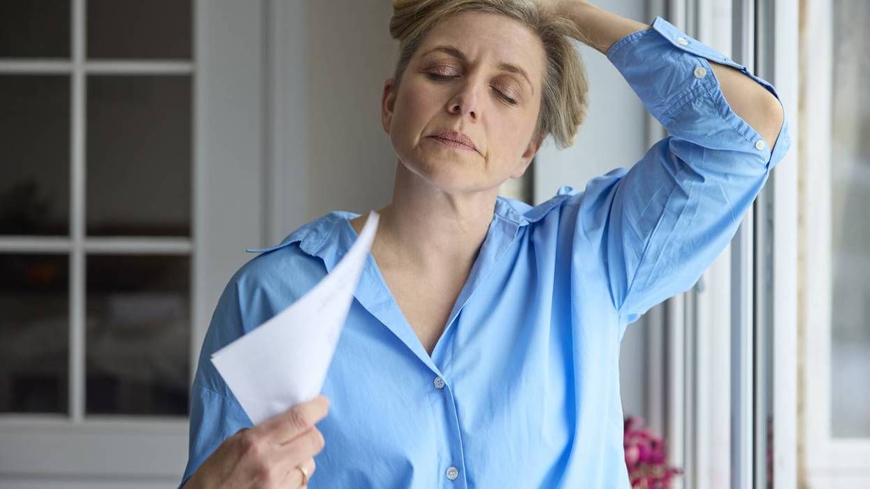Menopausal Mature Woman Having Hot Flash At Home Cooling Herself With Letters